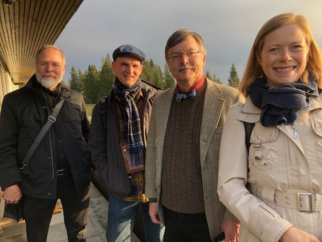 Tre menn og en dame står ute ikledd jakker og smiler mot kameraet.