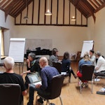 Bilde av folk som sitter oppdelt i grupper foran whiteboards på seminar