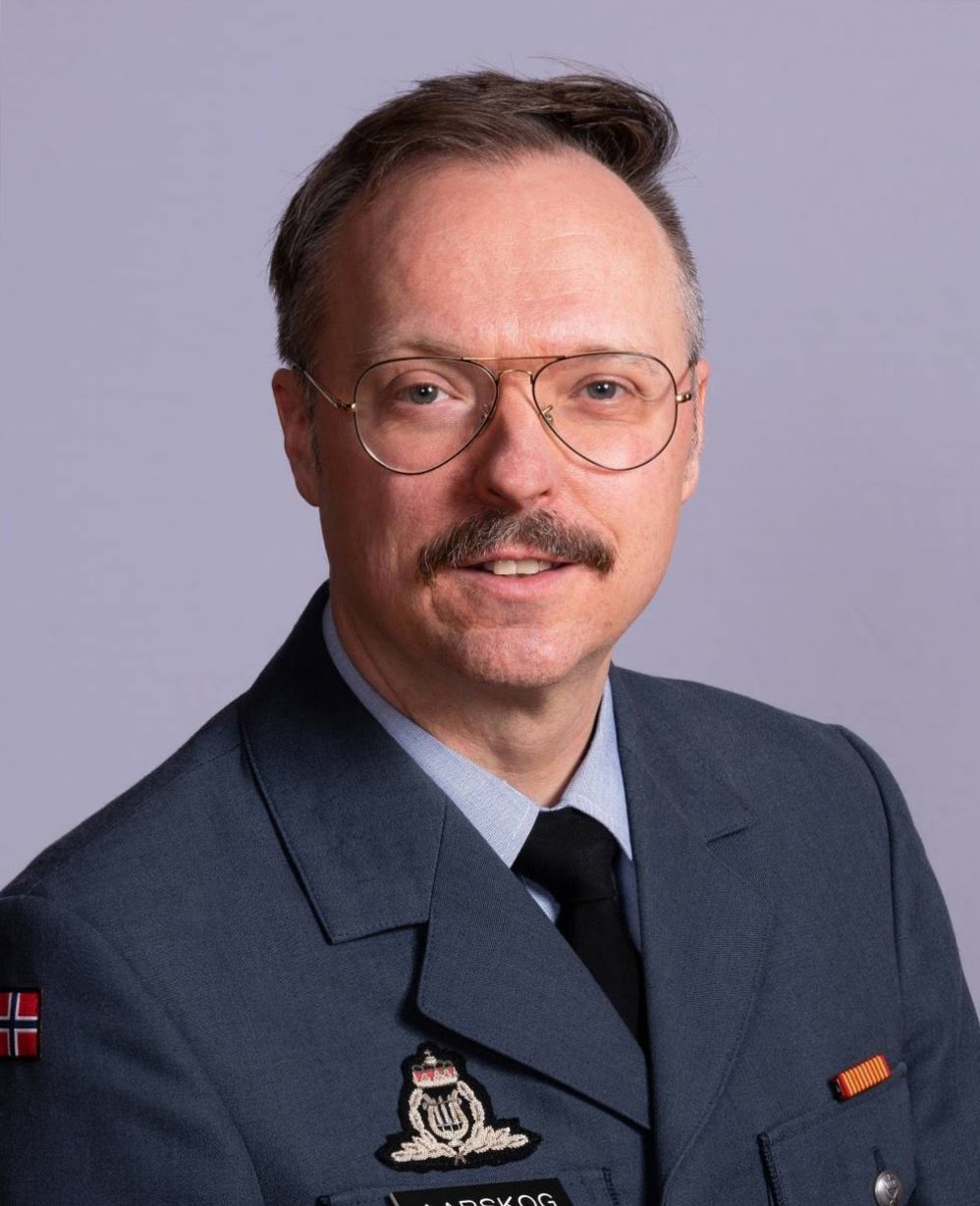 Hvit mann med bart og store briller ikledt blå jakke fra Luftforsvarets musikkorps og sort slips.