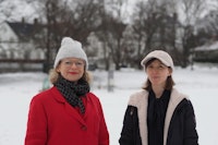 To kvinner. Hun til venstre med rød jakke, skjerf og hvit lue. Kvinnen til høyre med hvit cap og mørk jakke. Snø i bakgrunnen.