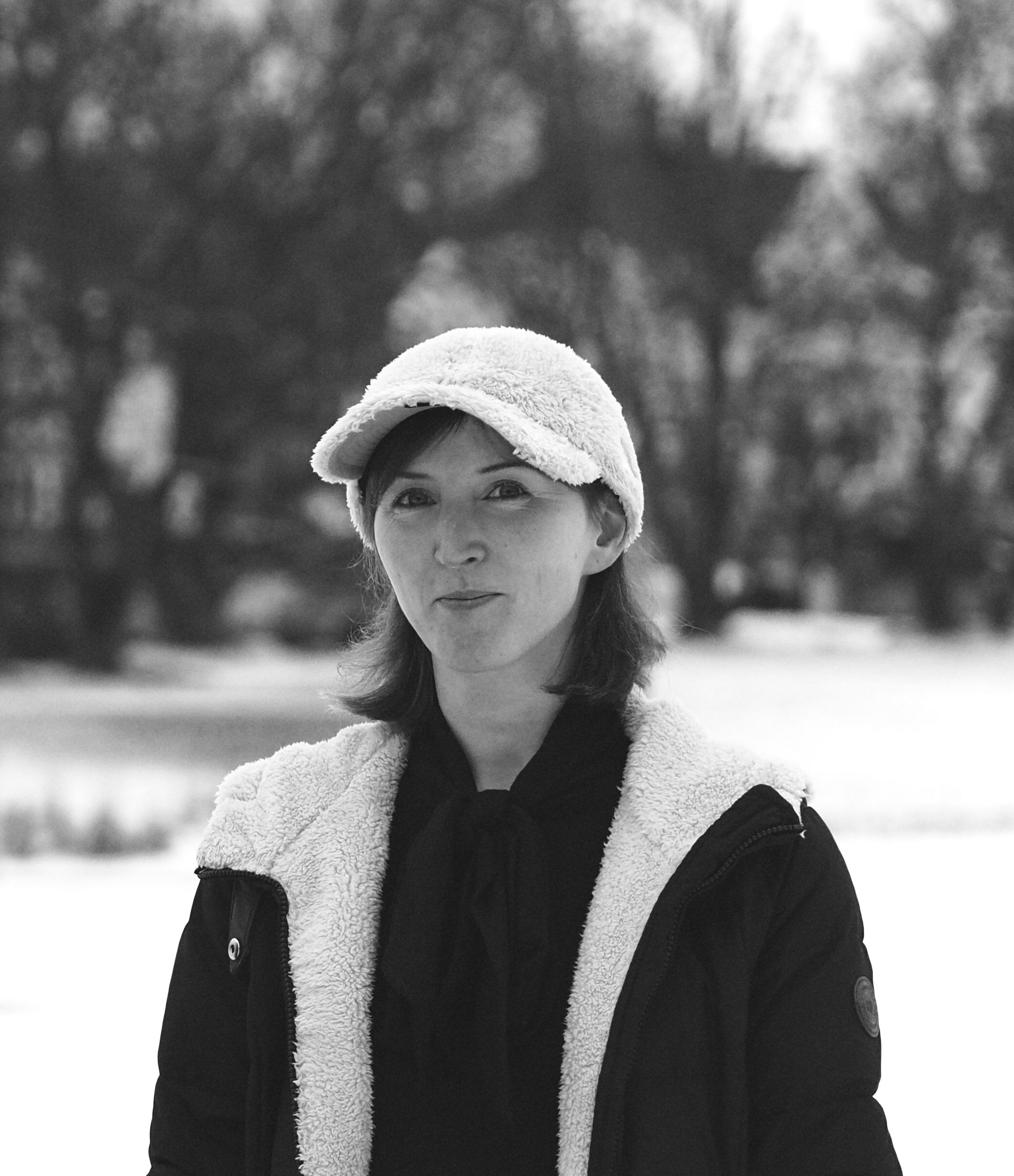Sort-hvitt bilde av kvinne med mørk jakke med lyst for fôr og hvit cap.