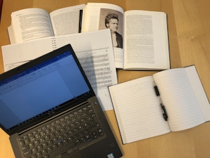 To pensumbøker og to notatblokker ligger oppslått på en bord. Ved siden av står en laptop med Word-programmet åpnet.