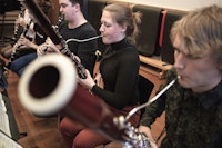 Fem studenter sitter på rad og rekke og spiller konsentrert på diverse treblåsinstrumenter.