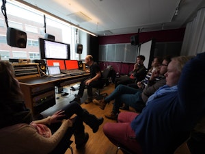 Fem studenter sitter i et lydstudio og ser på en lærer som jobber på datamaskinen med elektronisk musikk.