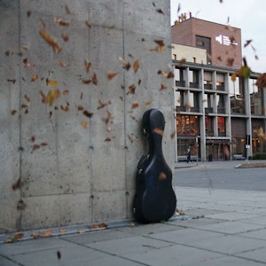 Gitarkasse står ved vegg, med blader som blåser rundt