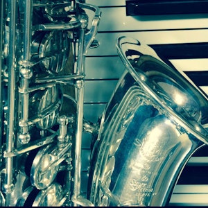 Saksofon-nærbilde foran pianobakgrunn