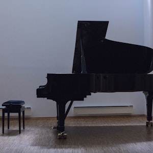 En flygel og en pianokrakk står i et ellers tomt rom.