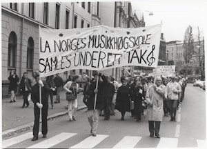 Demonstrasjonstog nedover gata. Banner hvor det står: La Norges musikkhøgskole samles under ett tak. Svart-hvitt.
