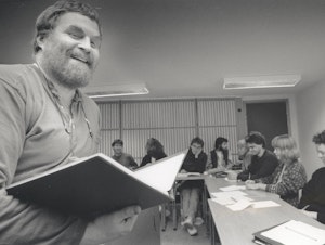 En smilende Olav Anton Thommesen foran studenter som sitter i hestesko i undervisningsrommet.
