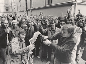 Harald Jørgensen og Einar Solbu spretter sjampanjen så den spruter foran mange glade mennesker. Feirer at vi får eget bygg i 1984.