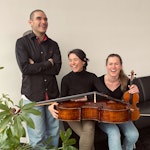 Trio med Ragna Rian, Mar Bonet Silvestre og Mario García Ramos sitter i sofaen utenfor administrasjonen med cello på fanget og fiolin i hånden.