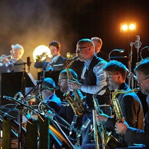 Konsertbilde av Bohuslän Big Band i mørk konsertsal med lys i bakgrunnen.