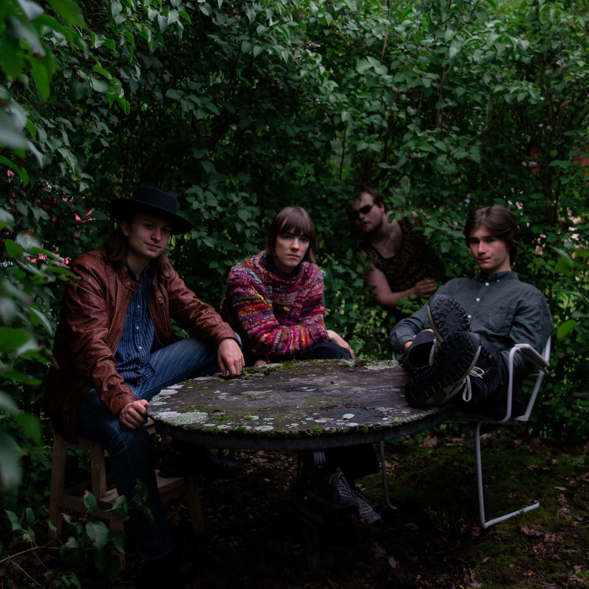 Bandet Dolkar sitter ved et rundt steinbord mellom mørkegrønne busker.