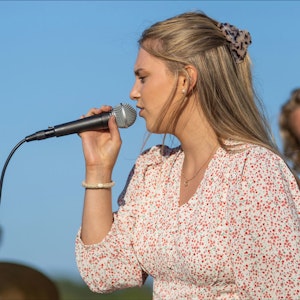 Emilie Iversen synger på scene foran blå himmel.