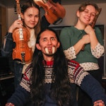 Gruppebilde av Saimi Kortelainen med hardingfele, Victoria Oftestad med fløyte og Adrian Lara med hoggtenner, mot konserten Eventyrstund fra Amazonas.