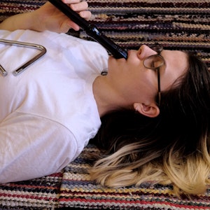 Astrid Solberg ligger på et teppe med et triangel på magen og spiller fløyte.