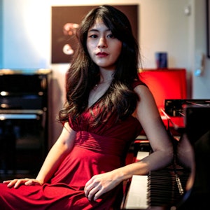 Grace Jee Eun Oh sitter i en knallrød kjole og lener seg på tangentene på et klaver.