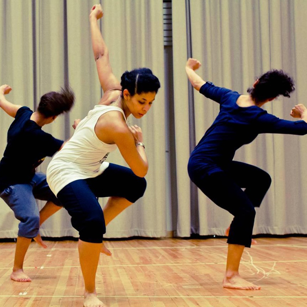 Tre dansere midt i en bevegelse med en fot og en arm opp.