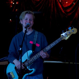 Joachim står på en scene og spiller på en el-bass og synger i en mikrofon.