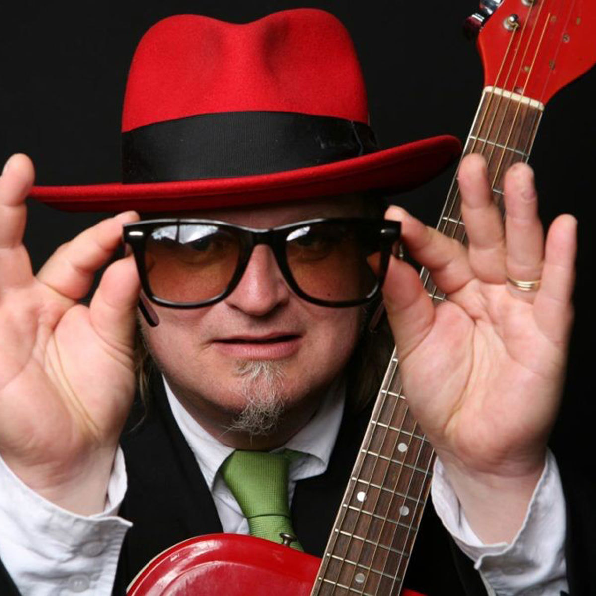 Portrett av Knut Reiersrud med rød hatt og gitar, og solbriller.