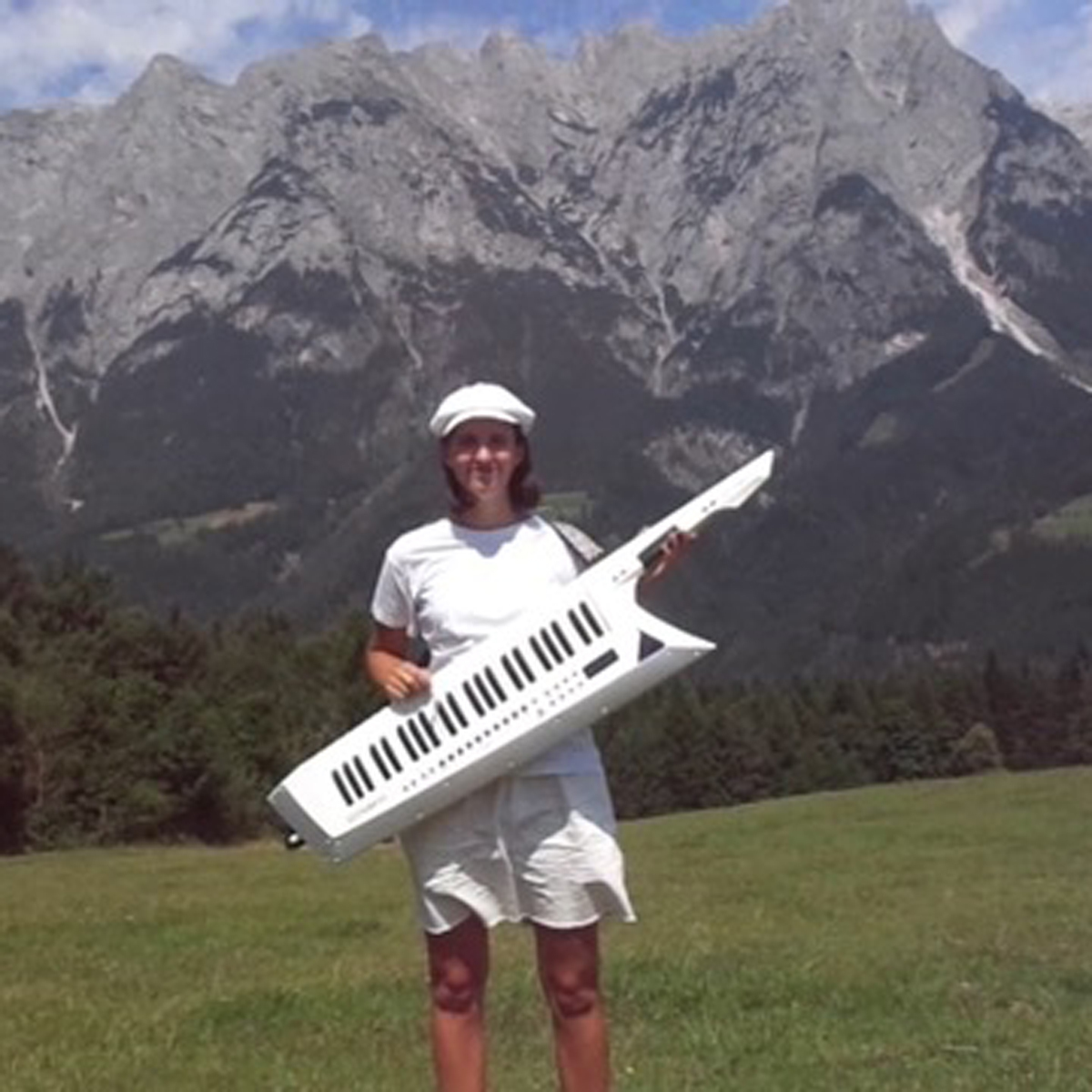 Leah Engevold står på en slette foran et fjell med gitar-pianoet sitt rundt halsen.