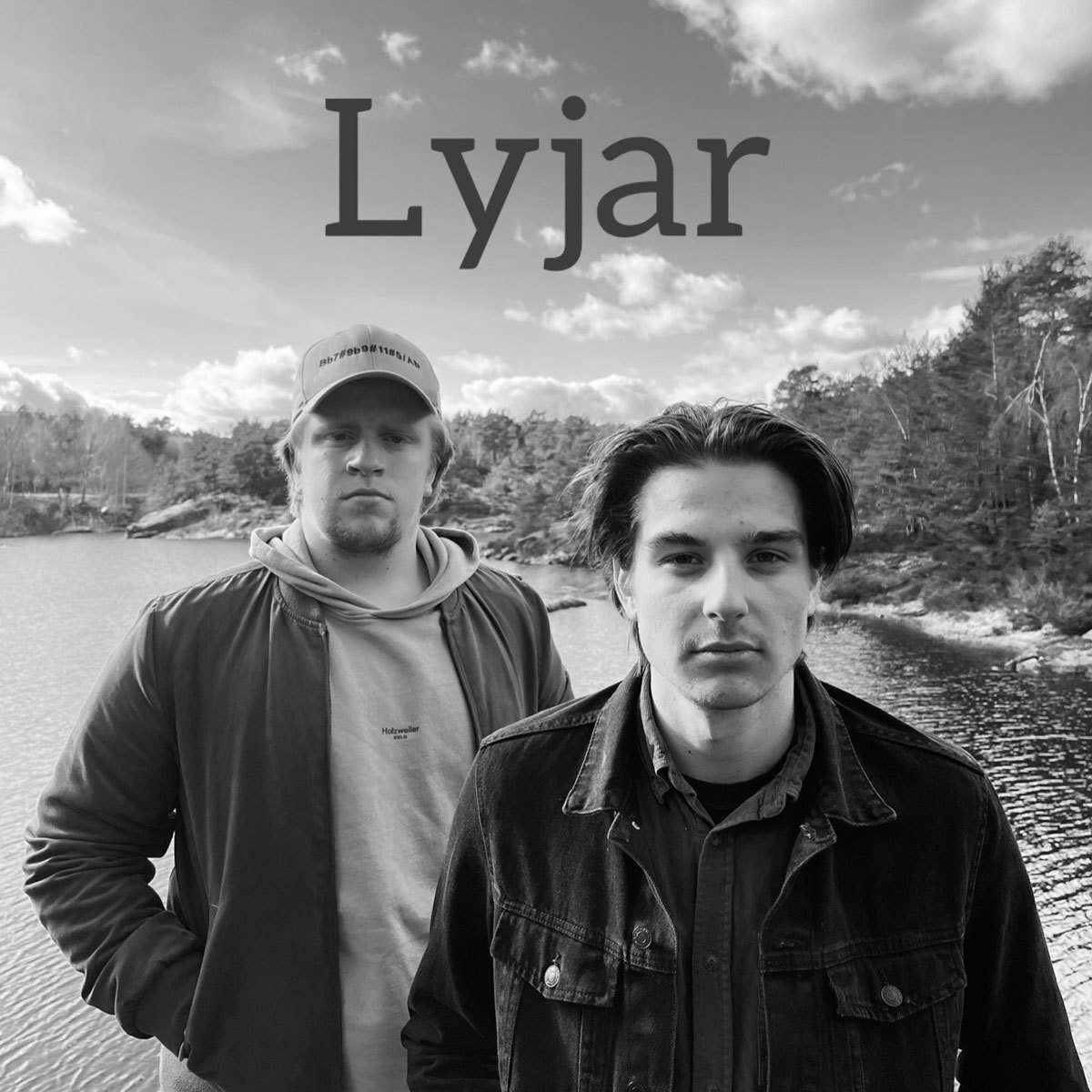 Musikerne i Lyjar står foran et vann, den ene litt foran den andre.