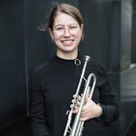 Monika Holst-Olsen står med trompeten i hånda og smiler.