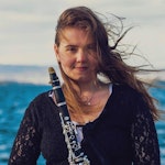 Morta Kacionaite med klarinett og vind i håret, foran blått hav.