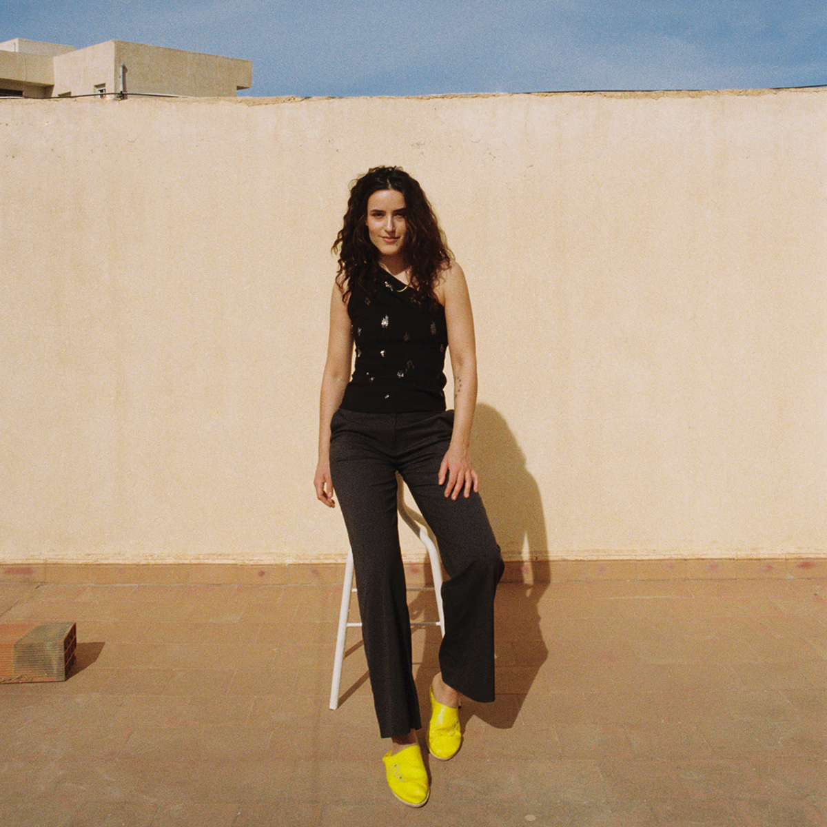 Nadia Essahli står foran brungul murvegg.