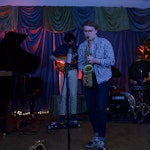 Oskar står på en scene og spiller saksofon inn i en mikrofon.