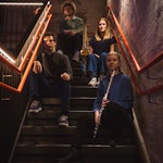 Gruppebilde av ensemblet Rugle som sitter i en litt mørk trapp.