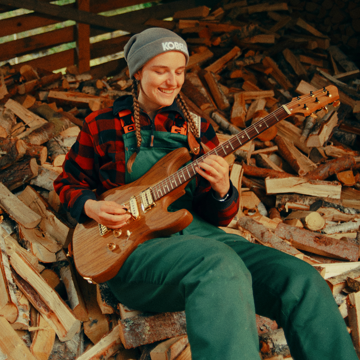 Symre Taugbøl Bang spiller gitar sittende oppå en haug med ved.