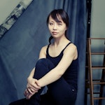 Pianist Sanae Yoshida sitter foran en blå gardin.