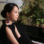 Sanae Yoshida sitter foran klaveret med grønne planter i bakgrunnen.