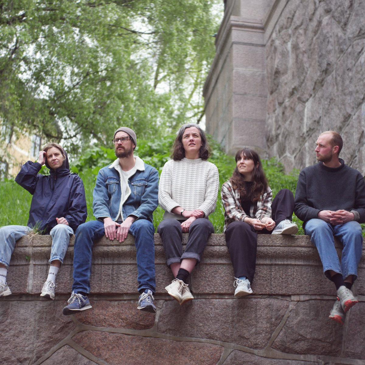 Musikerne i Sluppen Grafokordlag sitter på rad på en kant med beina hengene ned.