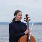 Sophia Hugo Cabo med cello, foran en fjord.