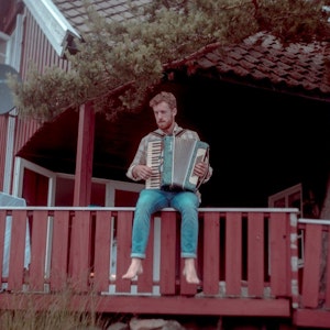Tobias Rønnevig sitter på et rødt terrassegelender og spiller trekkspill.
