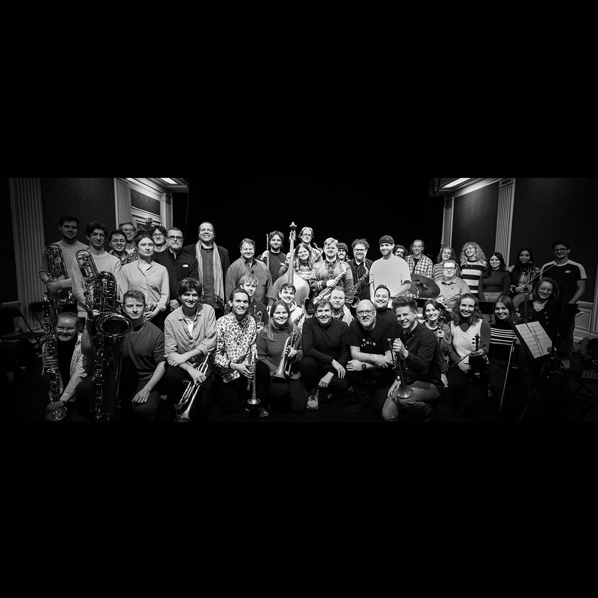 Stor gruppe musikere står i en gjeng og smiler.