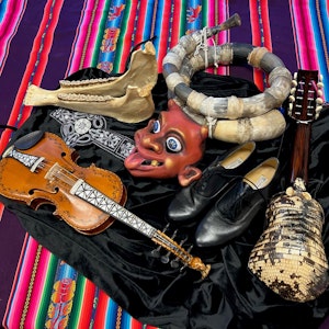 Hardingfele og flere tradisjonelle latinske folkeinstrumenter, en maske og sko, som ligger på et fargerikt teppe.