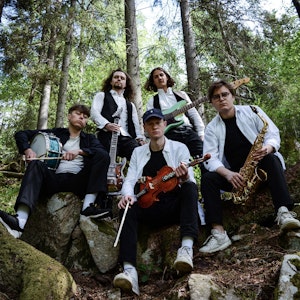 Musikerne i bandet Gangar sitter med instrumenter i en skog og ser ned i kameraet.