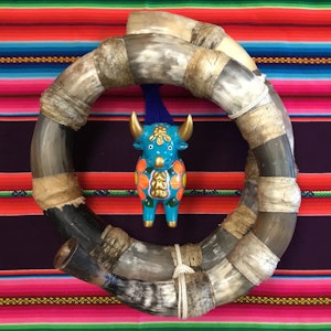 Et rundt håndlaget horn med liten oksefigur i midten, oppå et fargerikt teppe.