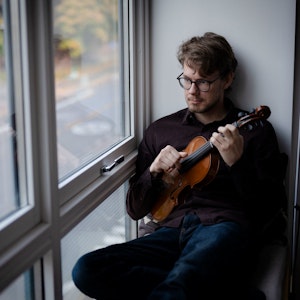 Jørgen Krøger Mathisen sitter i vinduskarm med fiolinen i hendene og ser ut.