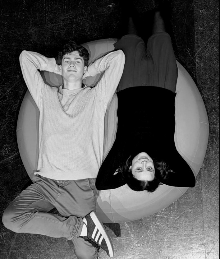 To personer som ligger fot mot hode på en stor puff, tatt ovenifra.