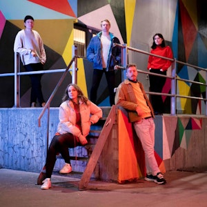 Musikerne i Elise Sløgedal band sitter spredt rundt på en opphøyning med en trapp. Veggen bak er i mange ulike farger