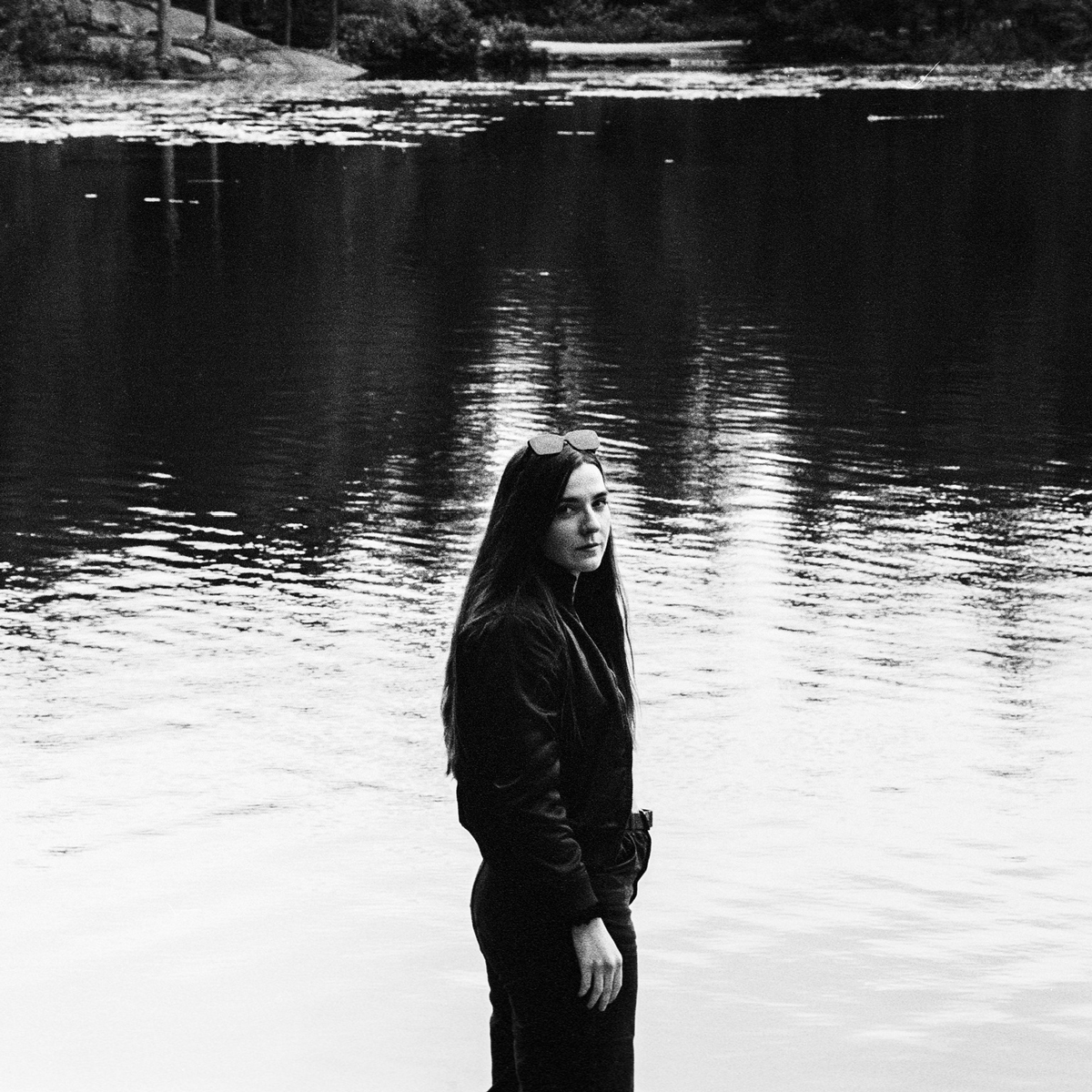 Svarthvitt-bilde av Tilla Gaasø som står foran et tjern og snur seg mot kamera.