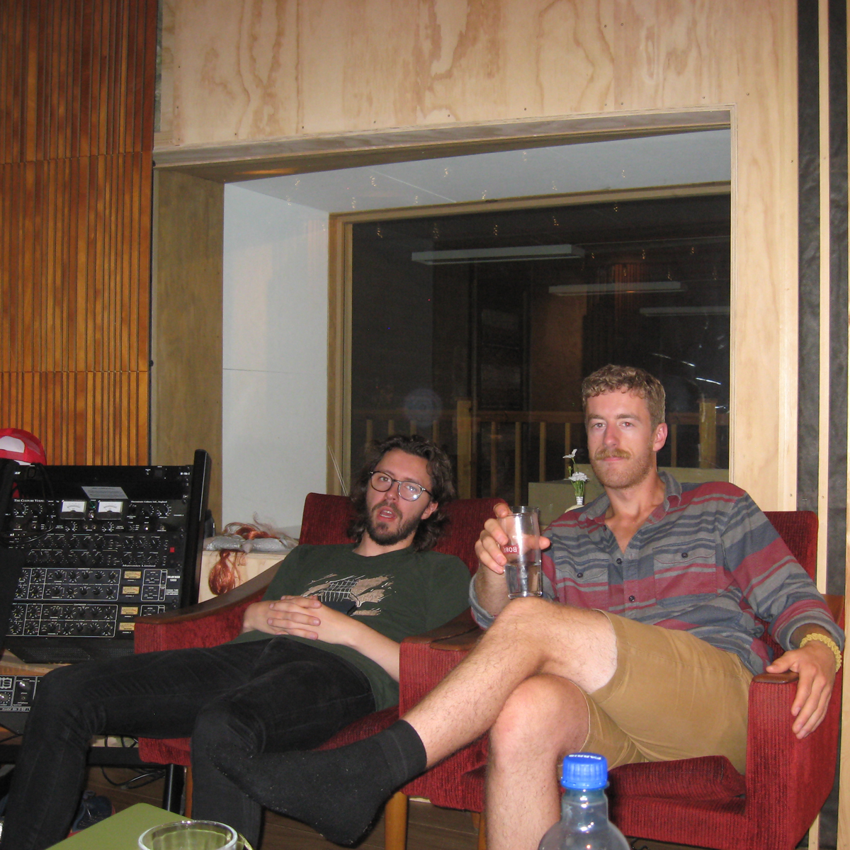 Tobias Rønnevig sitter i en rød sofa med et glass i hånden, sammen med en annen musiker. Det ser ut som et lydstudio.