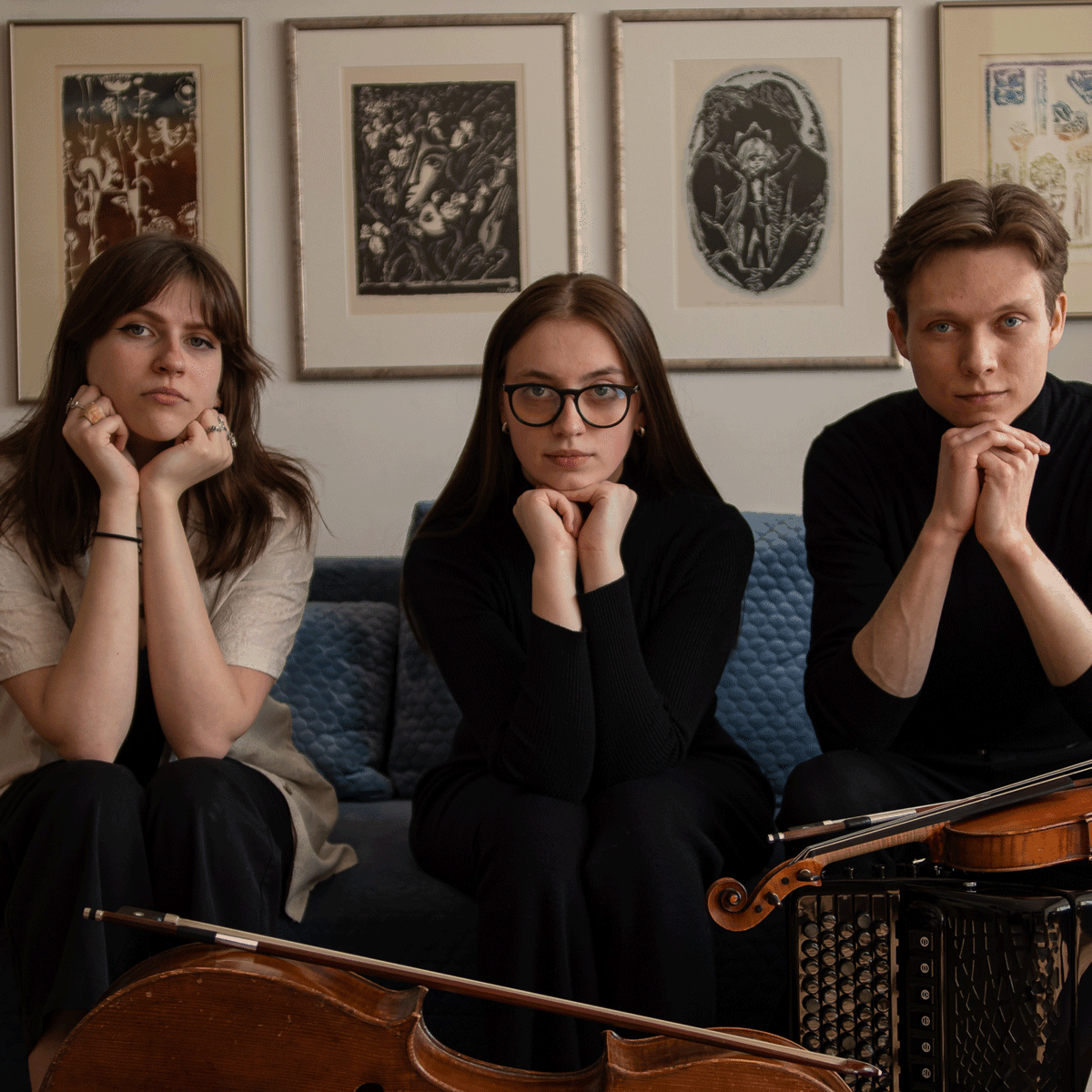 Musikerne i Trio Primavera sitter i en sofa med cello og fiolin, mens alle lener seg på hendene sine.
