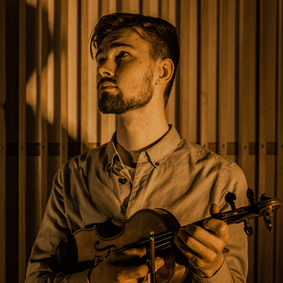 Trygve Liahagen står foran trevegg og ser ut i rommet med fela i hendene.