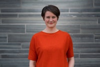 Bilde av Sarah-Jane Summers. Hun står foran en grå vegg ikledd rød genser.