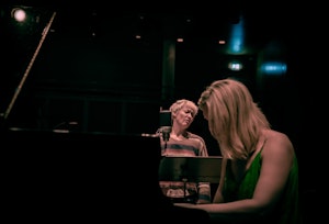 Live Maria Roggen sings in front of a microphone and Ingfrid Breie Nyhus plays the piano.